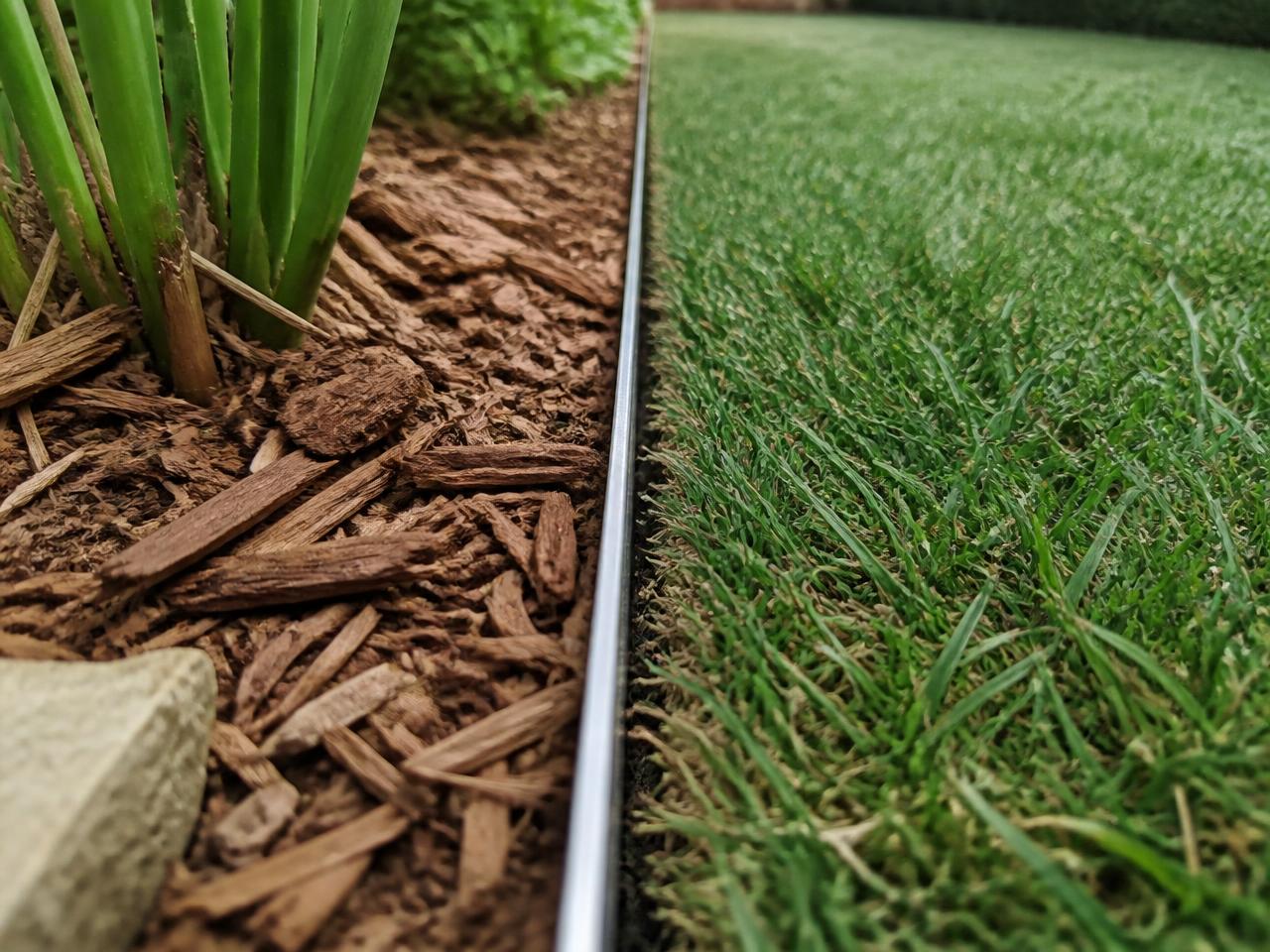 Close view of freshly laid sod with tight seams meeting an aluminum edge and cedar mulch